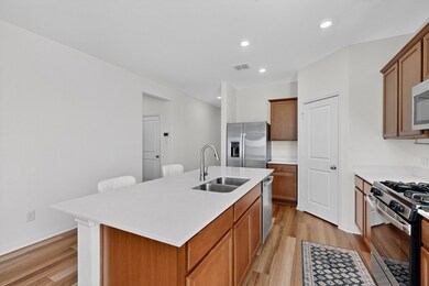 Kitchen featuring light wood-style flooring, appliances with stainless steel finishes, brown cabinetry, recessed lighting, and an island with sink