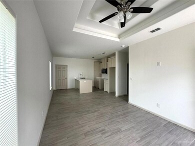 Unfurnished living room with light wood finished floors, visible vents, ceiling fan, baseboards, and a tray ceiling