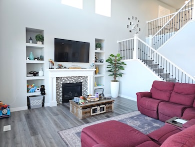 Living room with a fireplace, LVP floors, a towering ceiling, built in features, and stairs