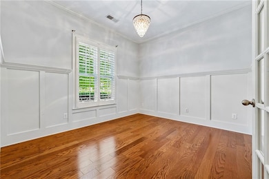 Unfurnished room with a decorative wall, wood finished floors, ornamental molding, wainscoting, and a chandelier