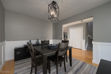 Dining area with wainscoting, stairway, a decorative wall, and light wood-style floors