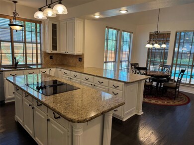Kitchen with black electric stovetop, decorative light fixtures, decorative backsplash, and kitchen peninsula