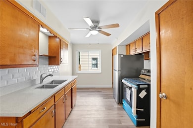 Kitchen featuring brown cabinets, appliances with stainless steel finishes, light wood-type flooring, a ceiling fan, and decorative backsplash