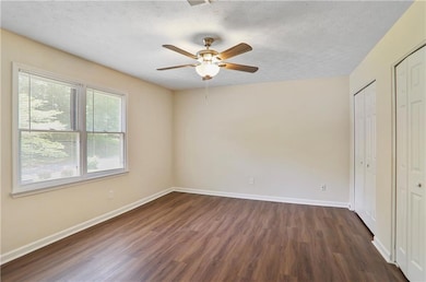 Unfurnished bedroom with multiple closets, dark wo