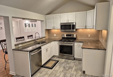 Kitchen featuring a breakfast bar, stainless steel appliances, lofted ceiling, dark stone countertops, and white cabinets