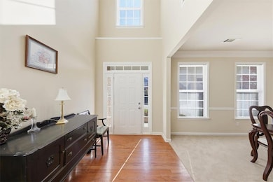 Foyer featuring light colored carpet, a high ceiling, light wood-type flooring, and ornamental molding