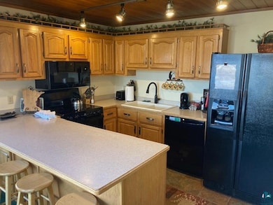 Kitchen featuring a peninsula, a sink, wood ceiling, light countertops, and black appliances