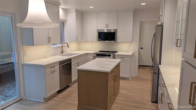 Kitchen with light stone counters, a kitchen island, stainless steel appliances, white cabinetry, and light wood-style flooring