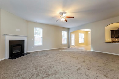 Unfurnished living room with a fireplace with flush hearth, carpet flooring, ceiling fan, and arched walkways