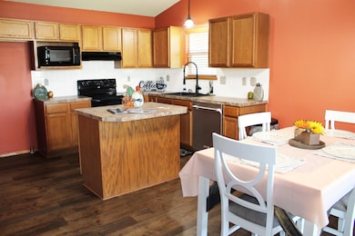 Kitchen featuring dark wood-style floors, black appliances, a center island, hanging light fixtures, and tasteful backsplash