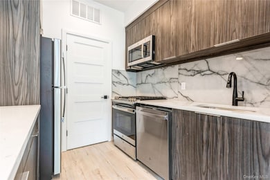Kitchen with stainless steel appliances, light wood-style flooring, modern cabinets, decorative backsplash, and light stone countertops.The pictures represent the model unit.