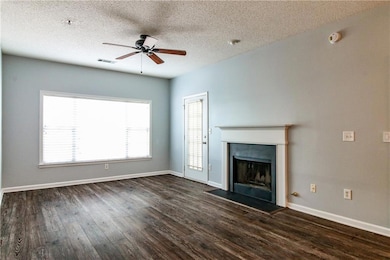 Unfurnished living room featuring ceiling fan, dark wood finished floors, a fireplace, and a textured ceiling
