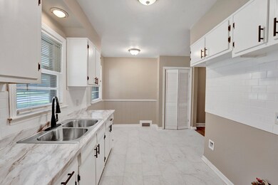 Kitchen with white cabinetry, sink, and light ston