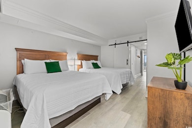 Bedroom with light hardwood / wood-style floors, a barn door, and crown molding