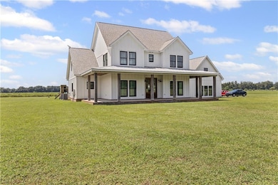 Modern farmhouse style home with board and batten siding, covered porch, a shingled roof, a front lawn, and a metal roof