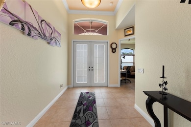 Foyer with light tile patterned floors, ornamental molding, and french doors