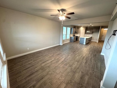 Unfurnished living room with ceiling fan, dark wood-type flooring, and sink