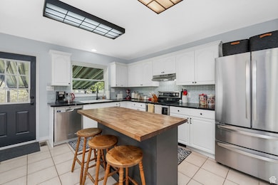 Kitchen with stainless steel appliances, white cabinets, light tile patterned floors, and a kitchen breakfast bar