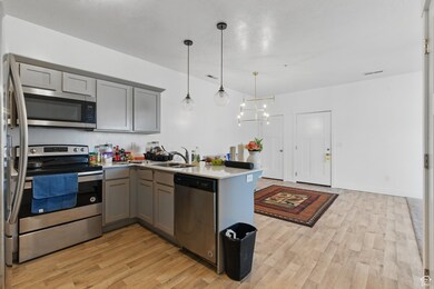 Kitchen with appliances with stainless steel finishes, gray cabinets, hanging light fixtures, and light countertops