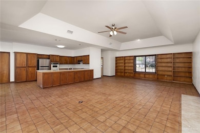 Kitchen featuring brown cabinetry, open floor plan, ceiling fan, freestanding refrigerator, and light countertops