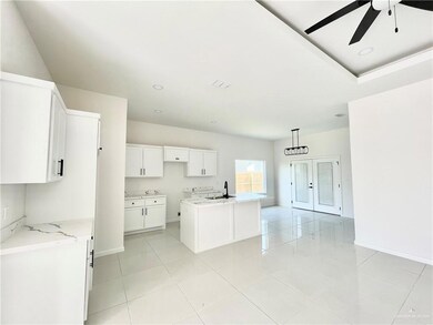 Kitchen with ceiling fan, light stone counters, white cabinets, sink, and a center island