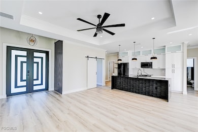 Unfurnished living room with a barn door, a raised ceiling, crown molding, light wood finished floors, and a ceiling fan