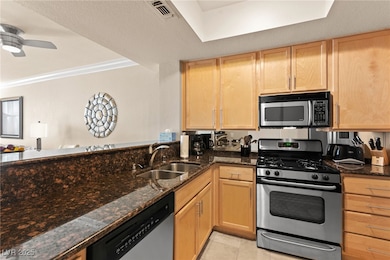 Kitchen featuring stainless steel appliances, dark stone counters, light tile patterned flooring, light brown cabinets, and crown molding