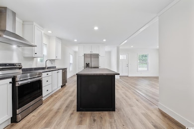 Kitchen with appliances with stainless steel finishes, wall chimney exhaust hood, dark countertops, a kitchen island, and white cabinets