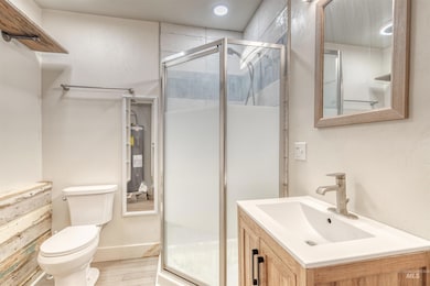 Full bath with water heater, vanity, a stall shower, wood finished floors, and recessed lighting