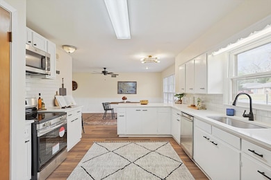 Kitchen with decorative backsplash, dark hardwood / wood-style floors, stainless steel appliances, sink, and white cabinetry