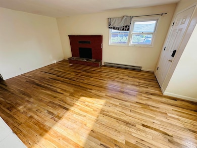 Unfurnished living room featuring a baseboard radiator, hardwood / wood-style flooring, and a brick fireplace