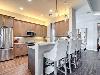 Kitchen with stainless steel appliances, a breakfast bar area, dark wood-type flooring, tasteful backsplash, and light countertops