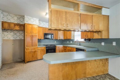 Kitchen featuring a peninsula, a sink, light countertops, brown cabinets, and black appliances