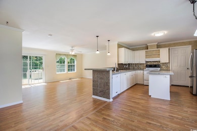 Kitchen featuring pendant lighting, open floor plan, dark wood-type flooring, white appliances, and ornamental molding