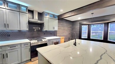 Kitchen with stainless steel gas stove, wall chimney range hood, pendant lighting, light stone counters, and sink
