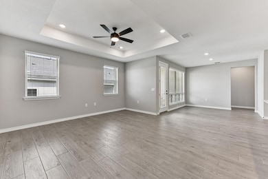 Unfurnished room featuring a tray ceiling, light wood-type flooring, recessed lighting, ceiling fan, and healthy amount of natural light