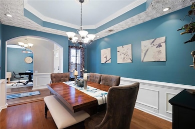 Dining space with a raised ceiling, a chandelier, crown molding, wainscoting, and a decorative wall