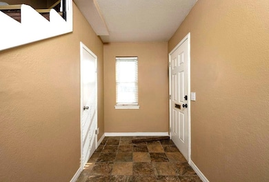 Corridor featuring a textured wall, stone finish flooring, and a textured ceiling