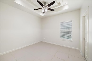 Empty room with a tray ceiling, light tile patterned flooring, and a ceiling fan