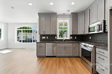 Kitchen with stainless steel appliances, light wood finished floors, gray cabinetry, backsplash, and plenty of natural light