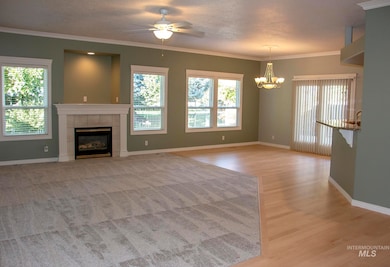 Unfurnished living room featuring crown molding, a tiled fireplace, light wood finished floors, a ceiling fan, and a chandelier