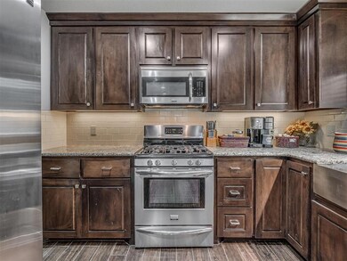 Kitchen featuring stainless steel appliances, dark wood-style flooring, dark brown cabinets, tasteful backsplash, and light stone counters