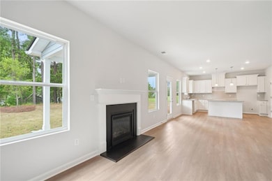 Unfurnished living room with plenty of natural light, light wood-style floors, a glass covered fireplace, and recessed lighting