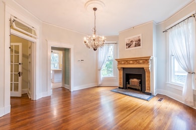 Unfurnished living room with wood finished floors, a chandelier, ornamental molding, and a tiled fireplace