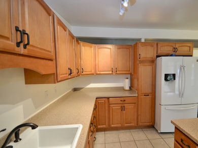 Kitchen with white refrigerator with ice dispenser, light tile patterned flooring, light stone countertops, and brown cabinets