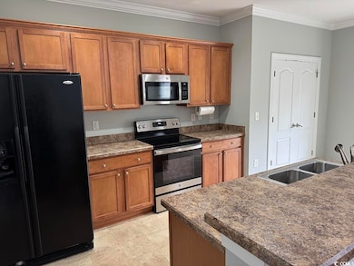 Kitchen featuring stainless steel appliances, brown cabinets, dark countertops, crown molding, and light tile patterned flooring
