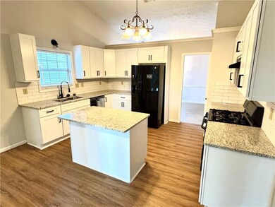 Kitchen with black appliances, backsplash, light stone counters, white cabinetry, and lofted ceiling