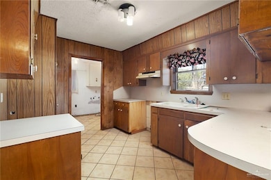 Kitchen with brown cabinets, light countertops, wood walls, light tile patterned flooring, and a textured ceiling