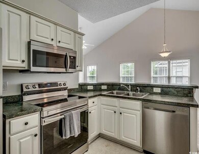 Kitchen featuring stainless steel appliances, hanging light fixtures, a textured ceiling, a peninsula, and high vaulted ceiling