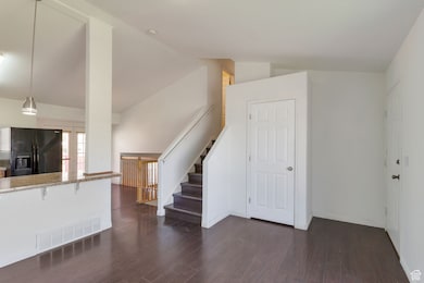 Unfurnished living room featuring dark wood-type flooring, stairs, and lofted ceiling